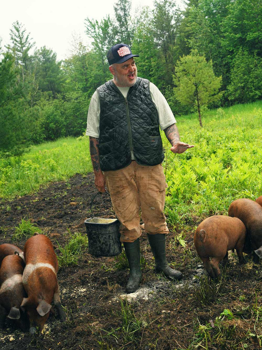 Man feeds pigs in a field while wearing Kamik Evermarsh waterproof work boots