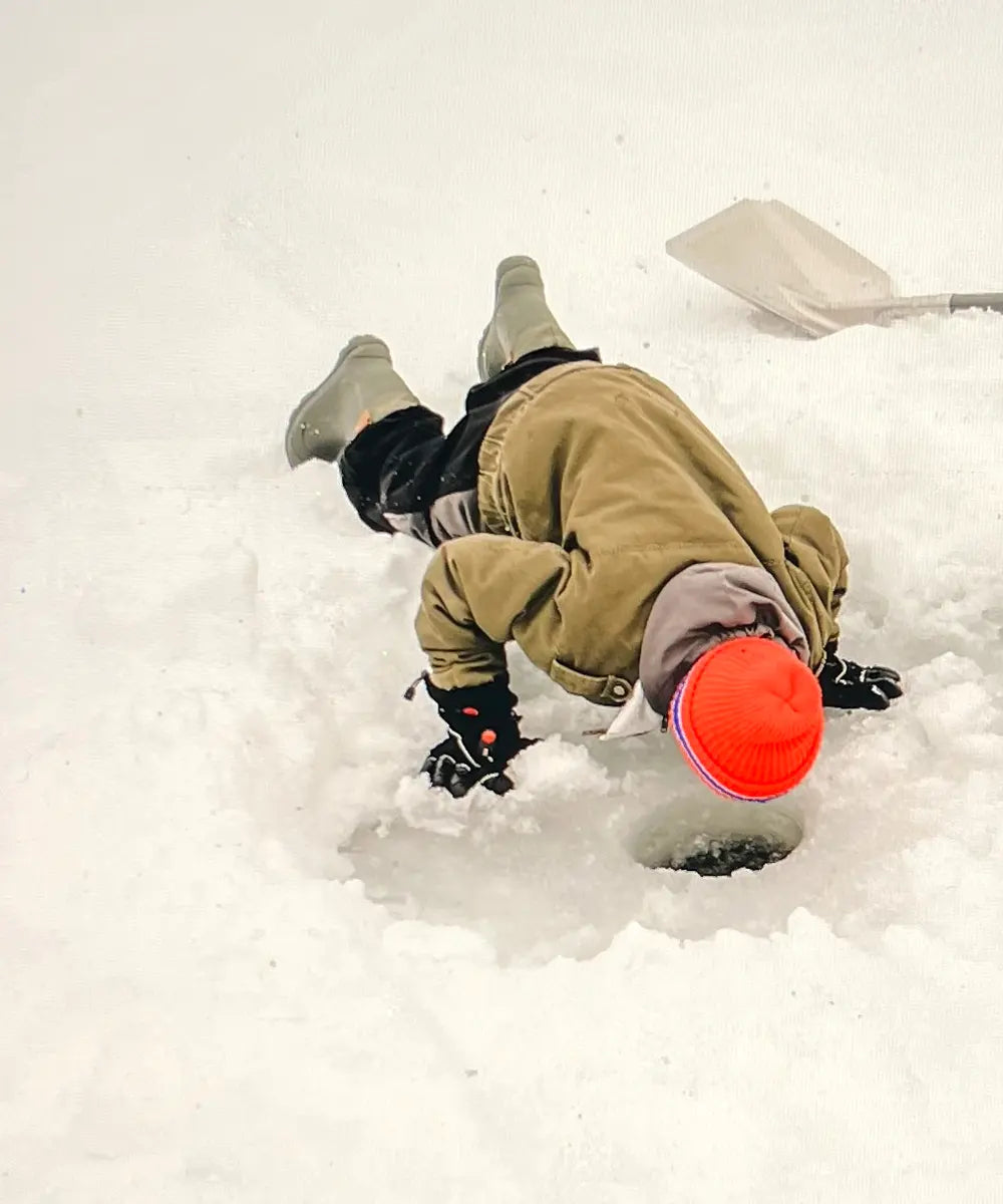 Kid peering into a fishing hole on a frozen lake while wearing Kamik Tundra Jr winter boots